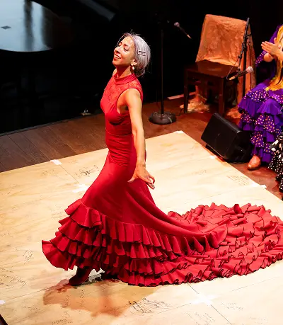 Flamenco dancer in a flowing red dress with dramatic ruffled train performing on wooden stage