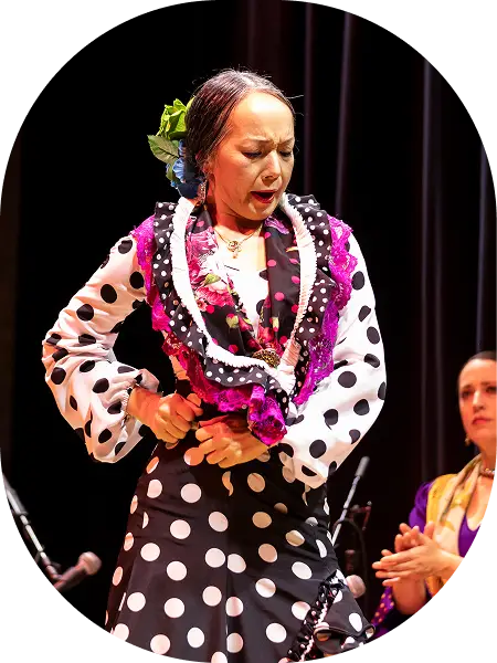 Flamenco dancer performing on stage wearing a black and white polka dot dress with purple accents, expressing intense emotion during a performance